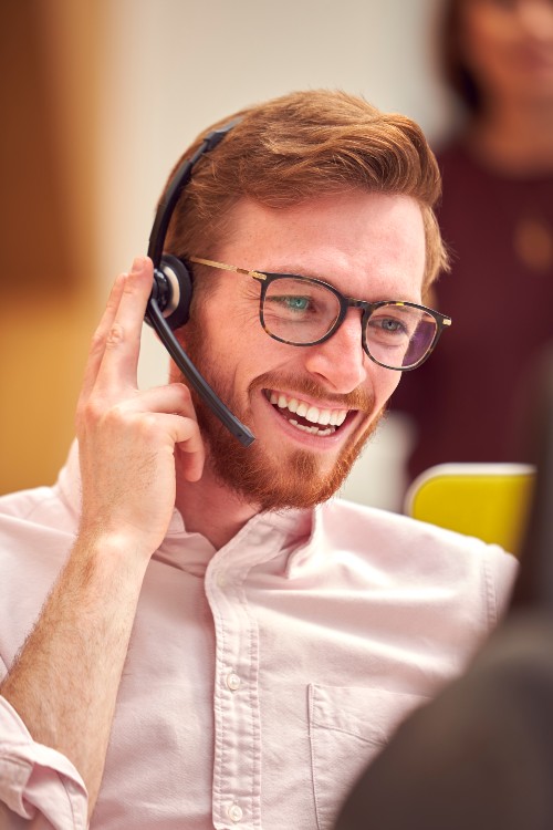 Man with glasses wearing a headset, seemingly in a cheerful mood, working for customer support at paltutors.